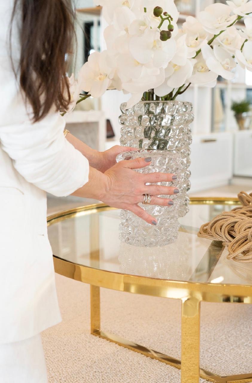 Vaso de cristal texturizado com orquídeas brancas sobre mesa de centro dourada