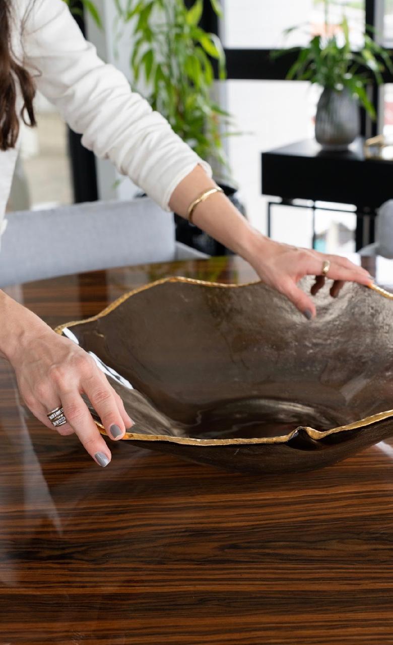 Centro de mesa escultural em bronze com borda dourada sobre mesa de madeira polida