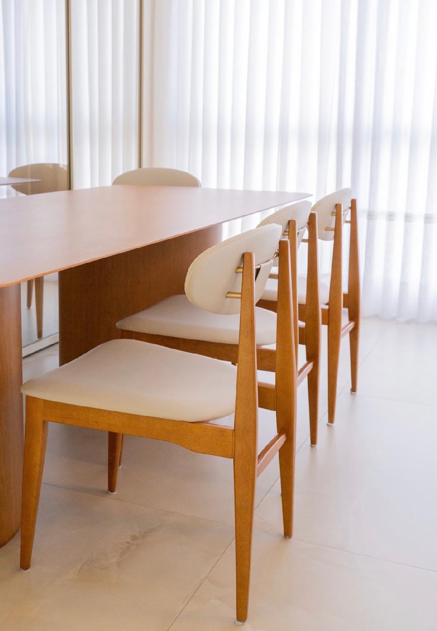 Mesa de jantar de madeira com cadeiras de encosto oval estofadas diante de cortina clara