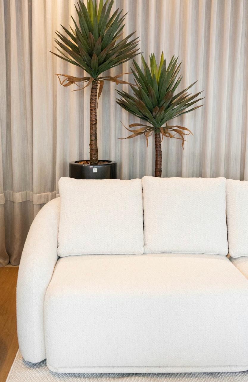 Sofá curvo em tecido bouclê off-white diante de cortina de linho e vasos com plantas
