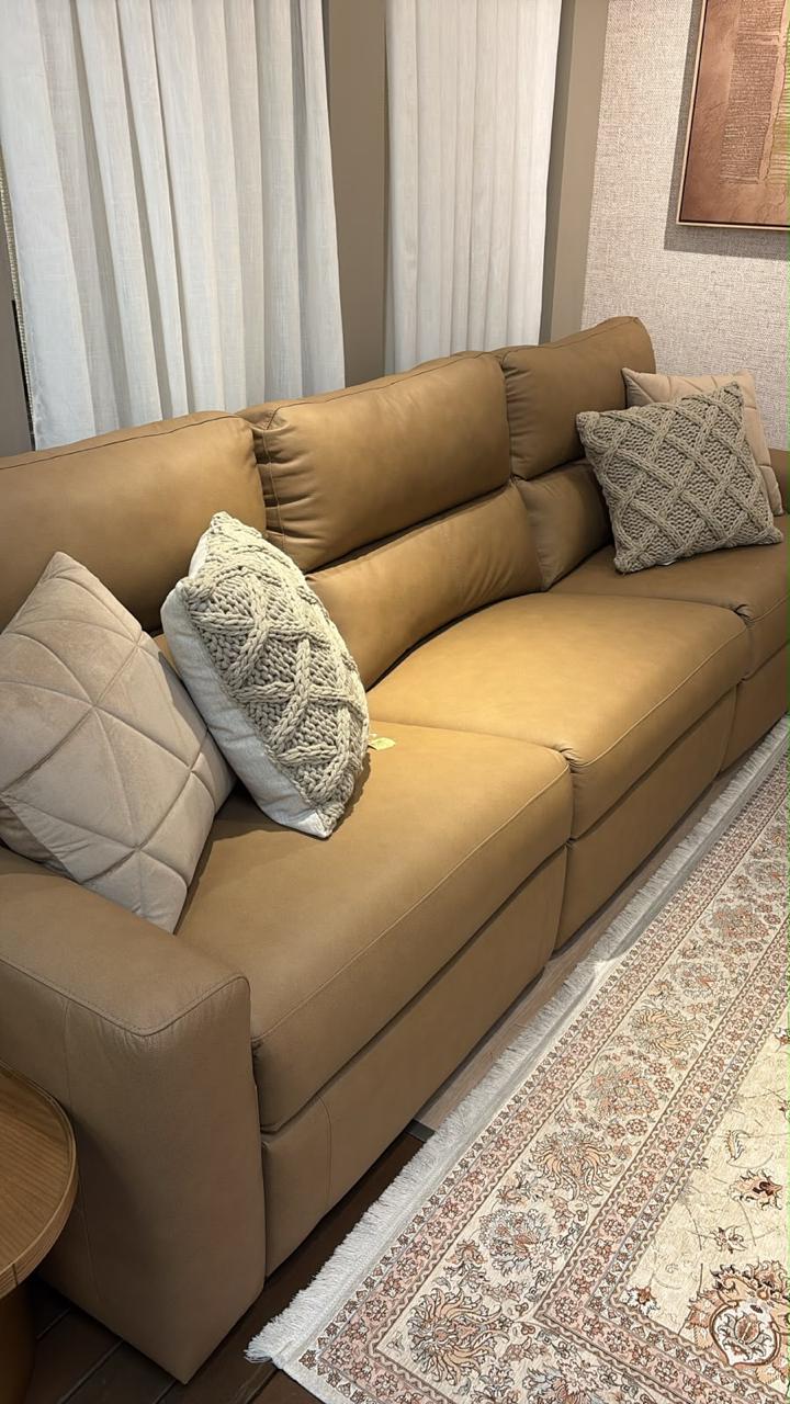 Cortinas de linho claro ao fundo de um sofá de couro com almofadas de tricô