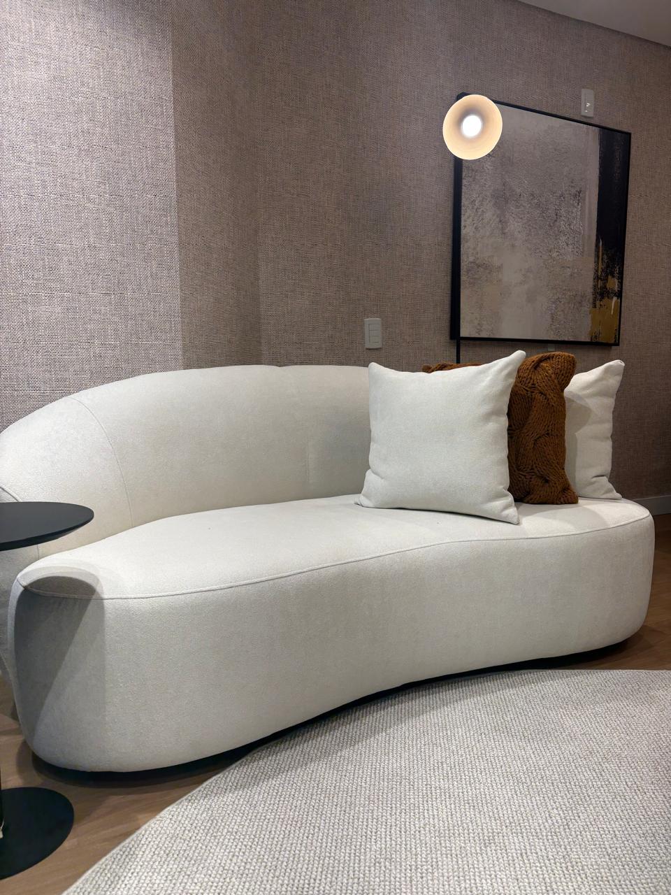 Sofá curvo orgânico off-white com almofadas claras e almofada de tricô caramelo