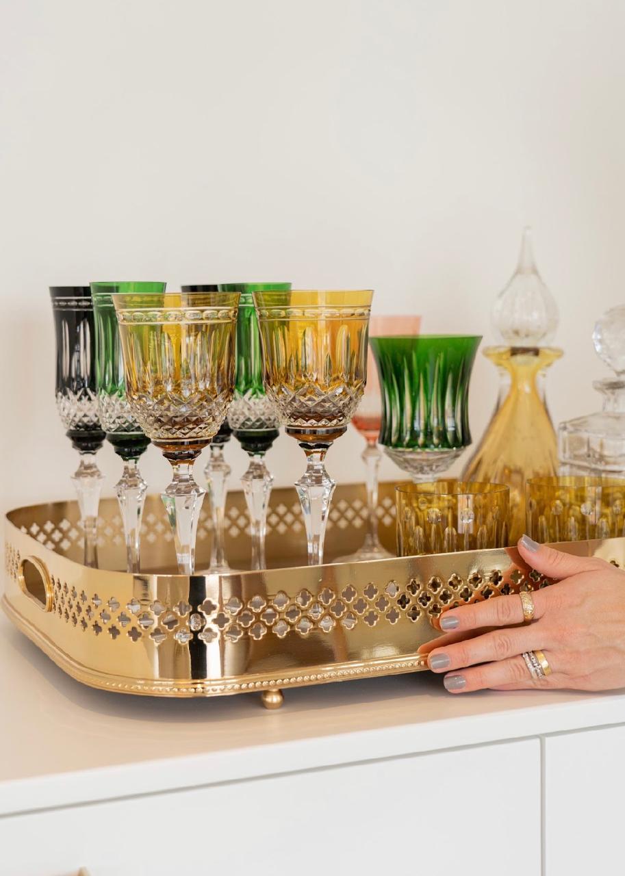 Taças de cristal coloridas sobre bandeja dourada vazada em aparador branco
